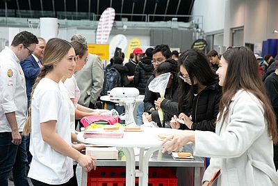 Im Vordergrund: Eine junge Frau mit Zopf berät ein Mädchen. Im HIntergrund sieht man noch unzählige Messebesucher auf der Lehrlings- und Lehrbetriebsmesse im Design Center Linz  ©Cityfoto.at/PELZL