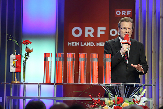 Moderator mit Mikrofon, im Hintergrund das ORF OÖ-Logo