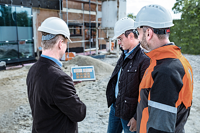 Drei Männer in Baustellenmontur mit Tablet auf Baustelle