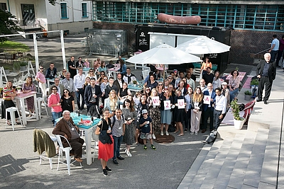Der 1. Geburtstag des International House des Welcome2Upper Austria Service Centers wurde mit einem Sommerfest in der Tabakfabrik Linz gefeiert. Die Teilenehmer stehen alle zusammen und lächeln in die Kamera ©cityfoto/Pelzl