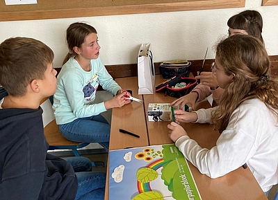 4 Kinder sitzen um einen Tisch im Klassenzimmer und bauen einen Roboter aus einer Milchpackung. 