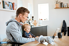 Vater sitzt mit seinem Baby am beim Laptop und arbeitet im Homeoffice ©iStock/Nomad