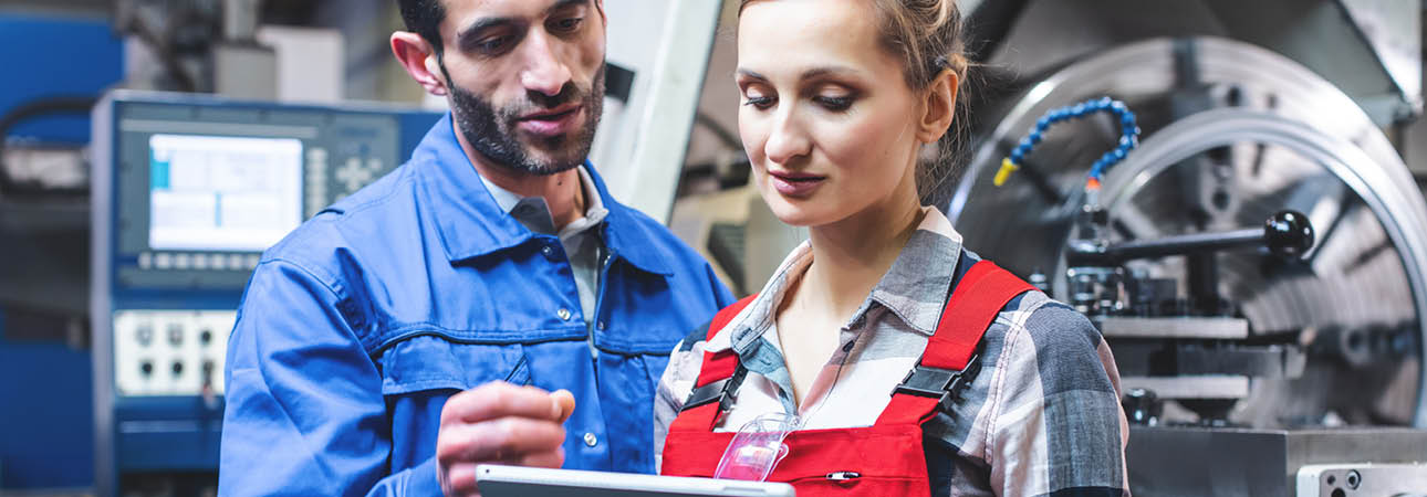 Männlicher Mitarbeiter in Blaumann bespricht sich mit einer Kollegin in rotem Arbeitsanzug©AdobeStock/Kzenon